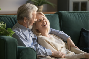 A senior couple sitting on a green couch in their Boca Raton home smiling and relaxing