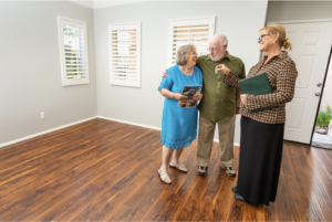 A senior couple and their realtor standing in the empty living room of their new apartment after downsizing from their larger home